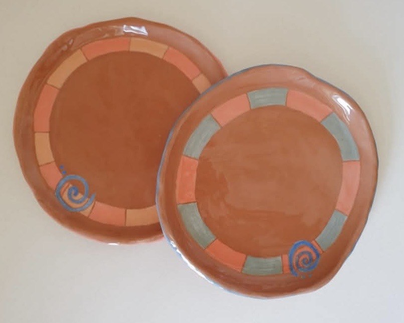 Two hand-painted terracotta plates with striped borders and spiral motif